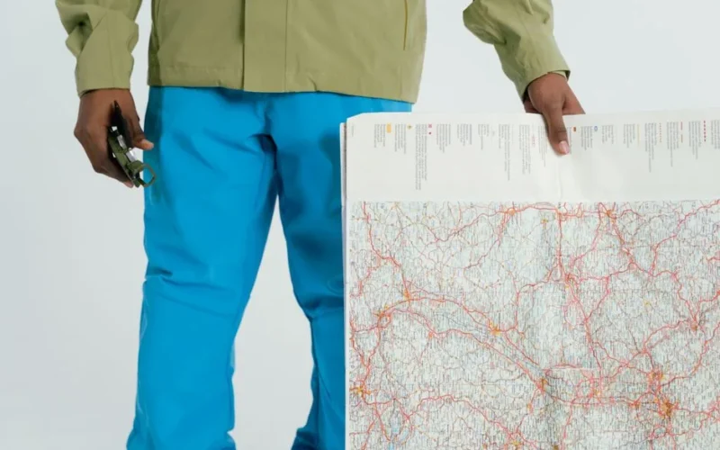 Man in outdoor attire holding a map and compass, prepared for exploration.