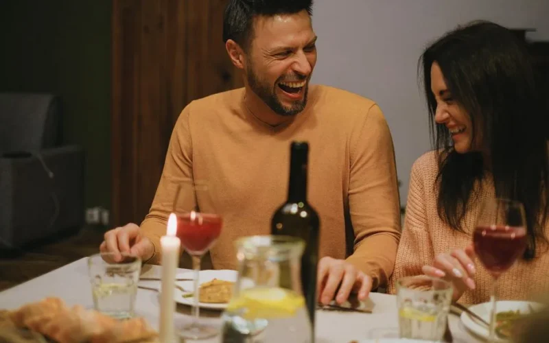 A joyful couple shares laughter and affection during a cozy dinner with wine and candlelight.