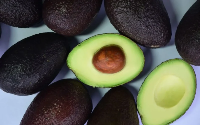 Top view of fresh avocados and cut halves on a white surface, showcasing their vibrant green color.