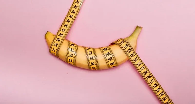 A banana wrapped with measuring tape on a pink background representing measurement or size concept.