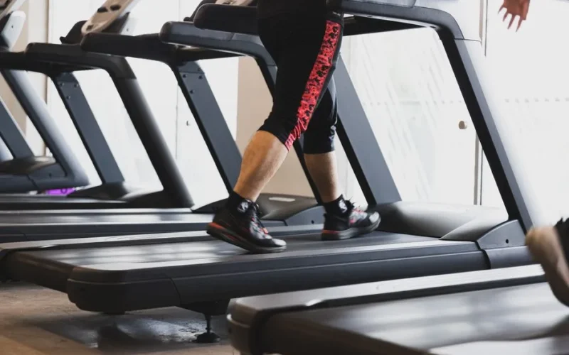 A person walking on a treadmill in a modern gym setting, focusing on fitness.