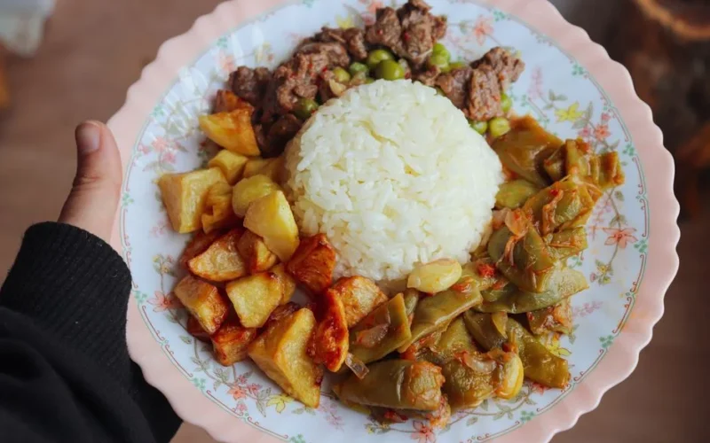 A close-up of a plate comprising white rice, roasted potatoes, sautéed green beans, and tender beef, offering a delicious meal.