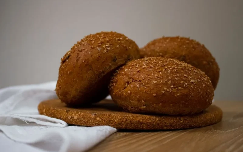 Freshly baked homemade brown bread rolls with seeds on a wooden board, perfect for healthy meals.