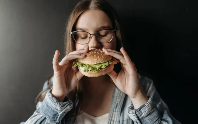 Young woman savoring a fresh burger indoors, depicting enjoyment of fast food.