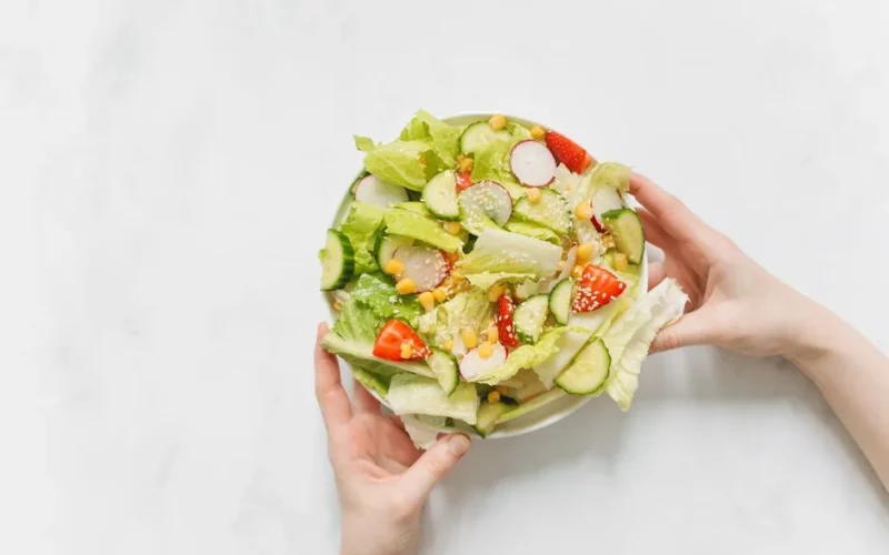 Hands holding a bowl of fresh vegetable salad with lettuce, cucumber, and radishes.