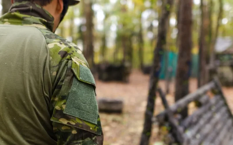 A soldier wearing camouflage preparing for a military exercise in a wooded outdoor environment.