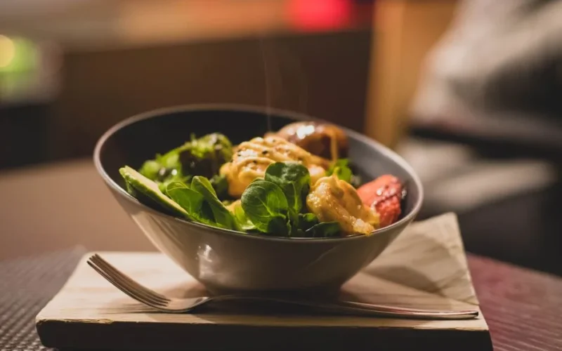 Delicious bowl of salad with fresh greens and grilled chicken served on a wooden platter.