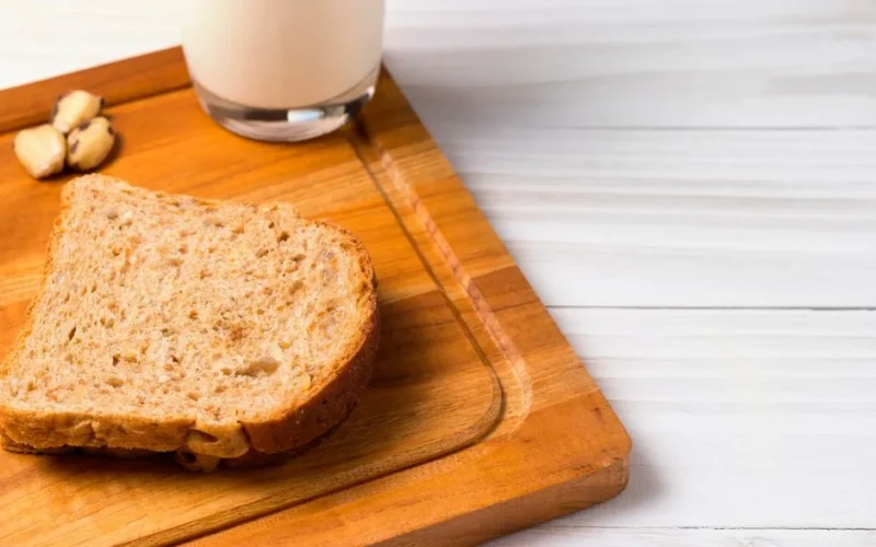 A close-up of a slice of whole wheat bread with a glass of milk, perfect for a healthy breakfast.
