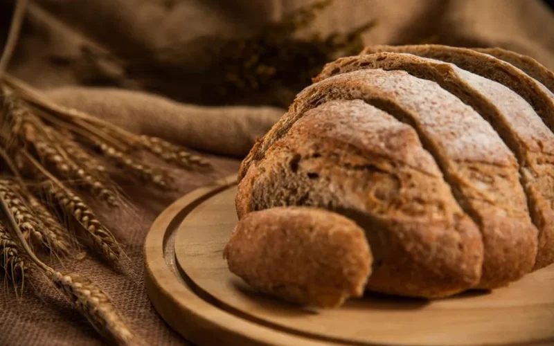 Freshly baked sliced bread on a wooden board with wheat grains for a rustic look.