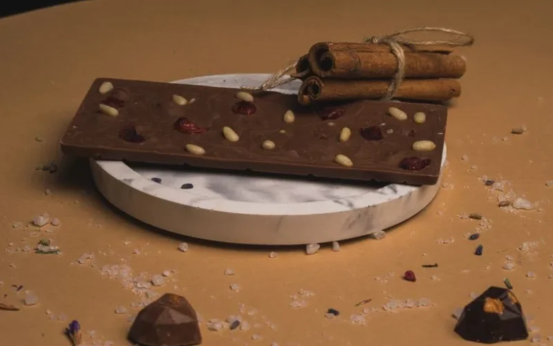 Delicious chocolate bar with nuts and berries on a marble plate, garnished with cinnamon sticks.