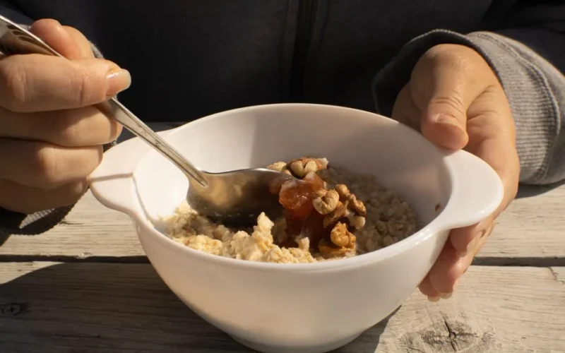 A bowl of oatmeal topped with walnuts and honey held by a person. Perfect nutritious breakfast option.