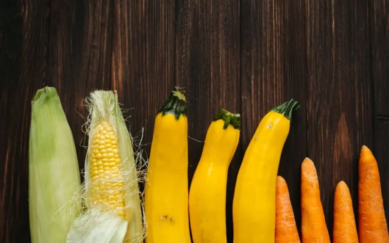 Colorful fresh corn, zucchini, and carrots arranged on a rustic wooden background.