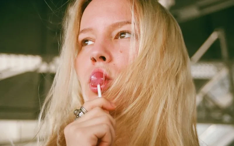 Close-up of a young woman with blonde hair enjoying a lollipop outdoors.