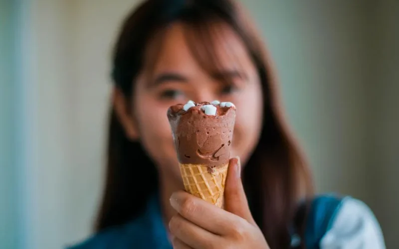 Soft focus of unrecognizable young Asian female with long brown hair showing tasty sweet chocolate ice cream cone in hand