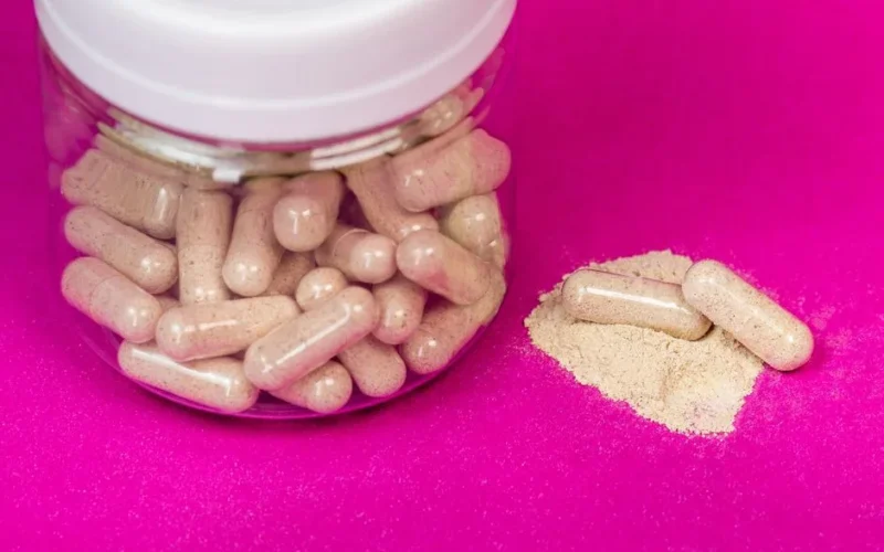 A glass jar filled with capsules alongside loose powder on a vibrant pink background.