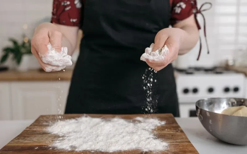 Close-up of hands sprinkling flour on a chopping board, ideal for food preparation themes.