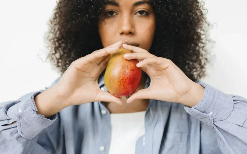 A woman in a blue shirt holds a ripe mango, blending fashion and food artfully.