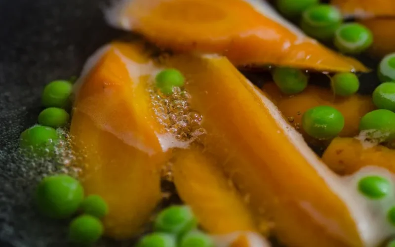 Close-up of carrots and peas boiling with bubbles in hot water, showcasing fresh vegetables.
