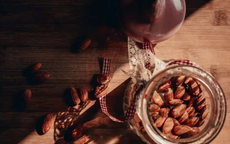 Rustic photo of almonds in a jar with warm lighting and shadows on a wooden table.