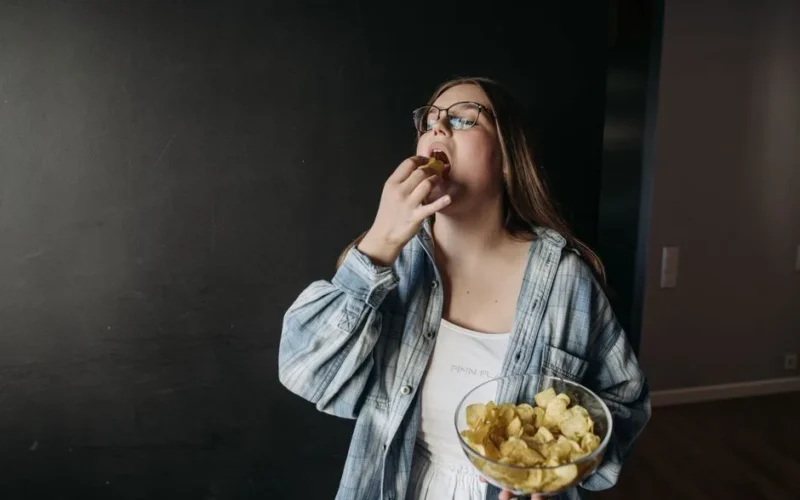 Young woman eating potato chips indoors, enjoying a snack moment.