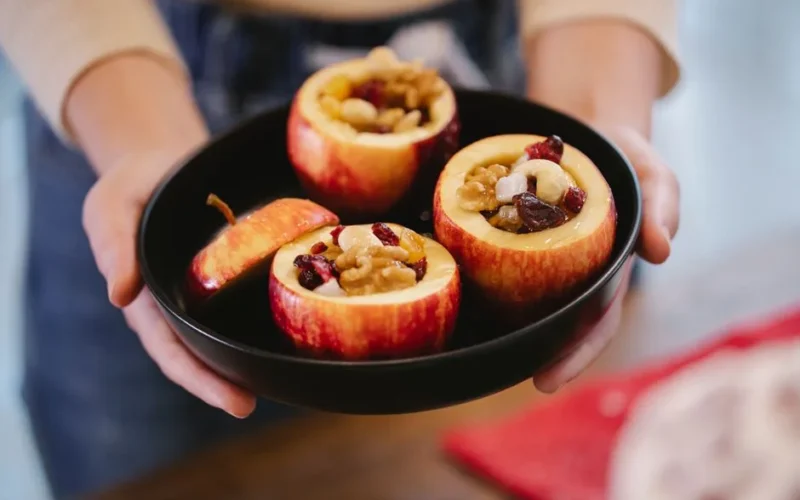 Crop anonymous female cook showing baking pan with appetizing baked apples filled with nuts and dried cranberries at home
