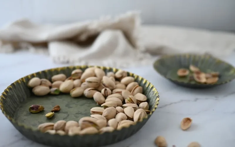 Close-up shot of pistachios in a rustic green bowl on a marble surface.