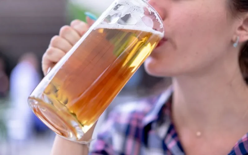 A woman enjoying a lager beer from a clear glass mug. Perfect for lifestyle and beverage-related content.