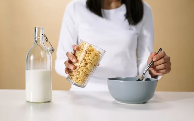 Person pouring cereal into a bowl with a bottle of milk nearby, ready for breakfast.