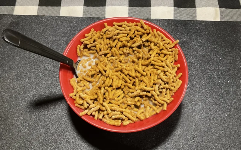Photograph taken of Fiber One Original Bran cereal in a bowl of milk with a black spoon on a table.