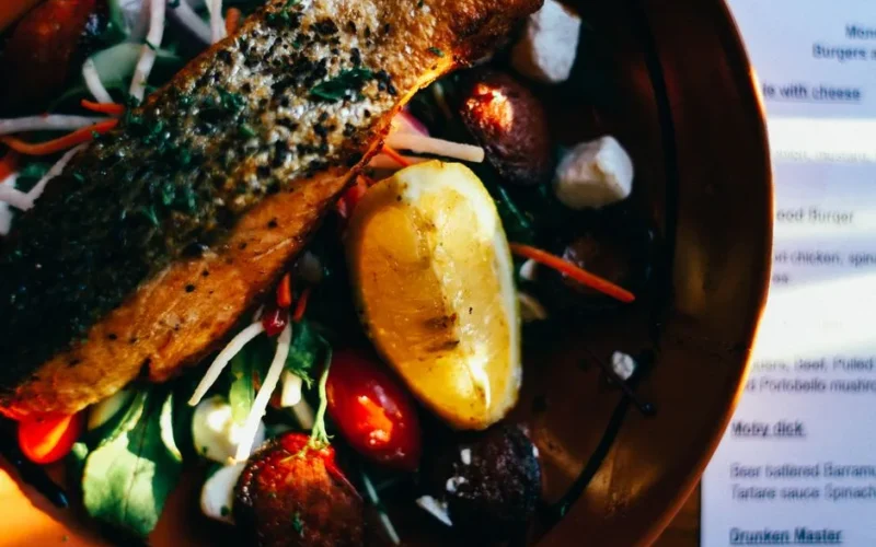 Close-up of a grilled salmon salad garnished with fresh vegetables and lemon.
