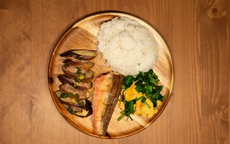 Delicious Asian dish with rice, grilled fish, and vegetables on a wooden plate.