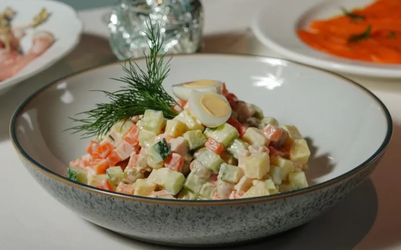 Colorful vegetable salad garnished with dill and quail eggs in a speckled ceramic bowl.