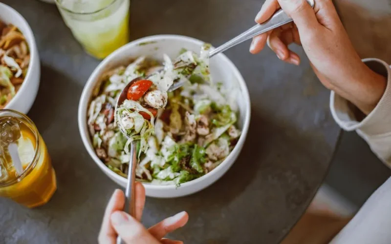 A person enjoying a fresh salad with cherry tomatoes and greens indoors.