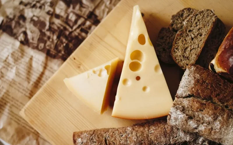 Close-up of cheese and rustic bread on a wooden board, ideal for culinary themes.