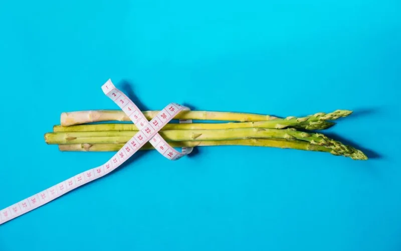 Fresh asparagus wrapped with measuring tape on a vibrant blue background.
