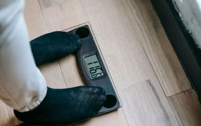 From above of unrecognizable person in socks standing on electronic weighing scales while checking weight on parquet during weight loss