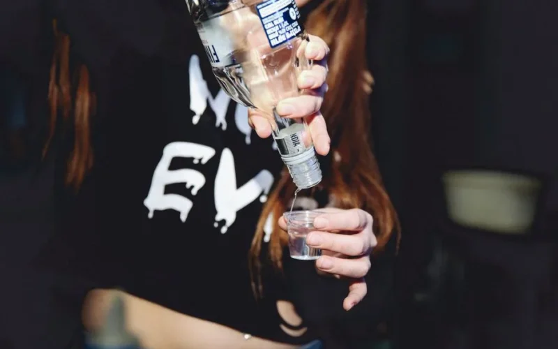 A woman pours vodka into a shot glass during a night gathering, symbolizing nightlife and celebration.