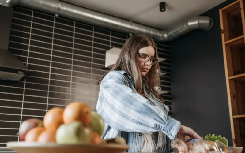 Woman in casual plaid shirt preparing food with fresh ingredients in modern kitchen.