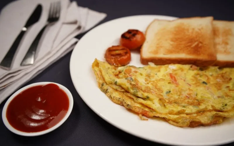 A hearty breakfast featuring omelette, toast, grilled tomatoes, and ketchup on a black background.