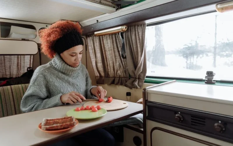 A woman chops cherry tomatoes in a camper van kitchen, showcasing a cozy van life scene.