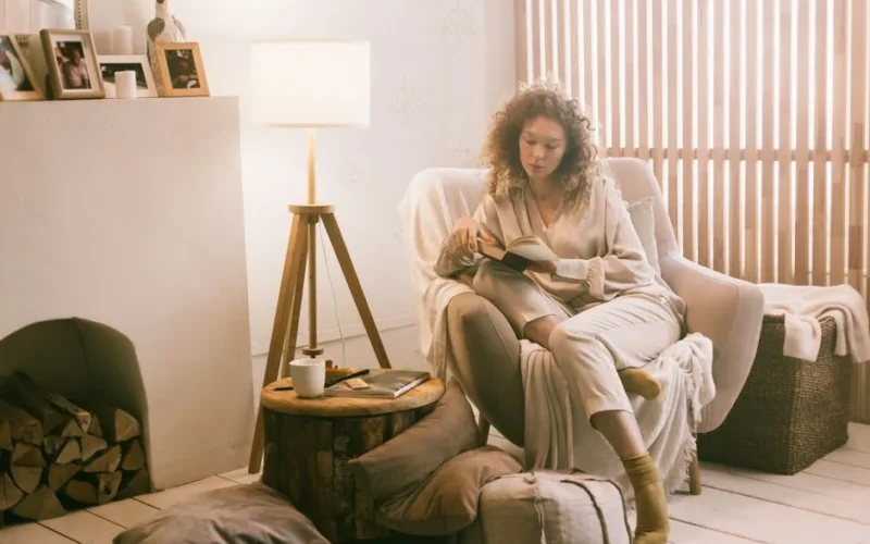 Woman relaxing in a cozy armchair at home, enjoying a book in a warmly lit room.