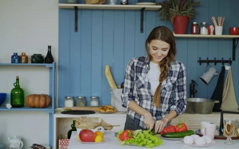 Smiling woman chopping vegetables in a cozy kitchen setting.