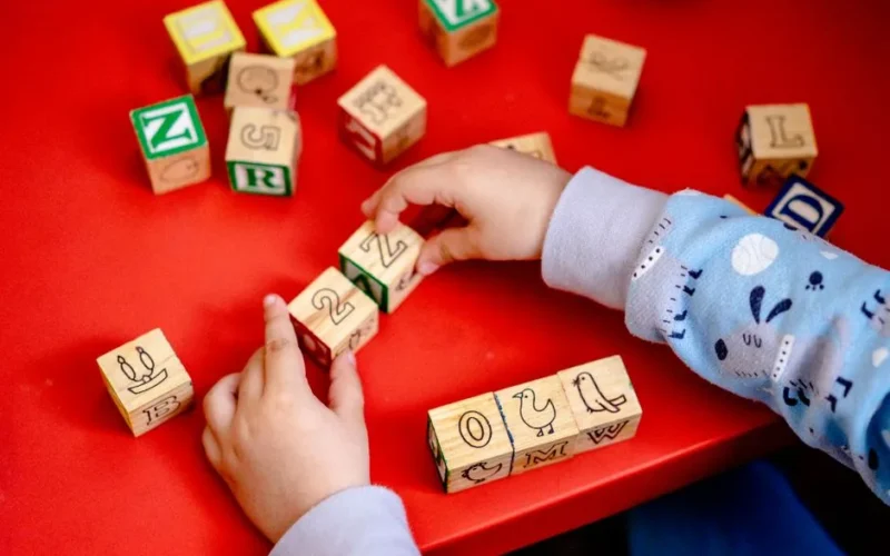 Young child engaging with wooden alphabet blocks on a vibrant red table, learning and playing.
