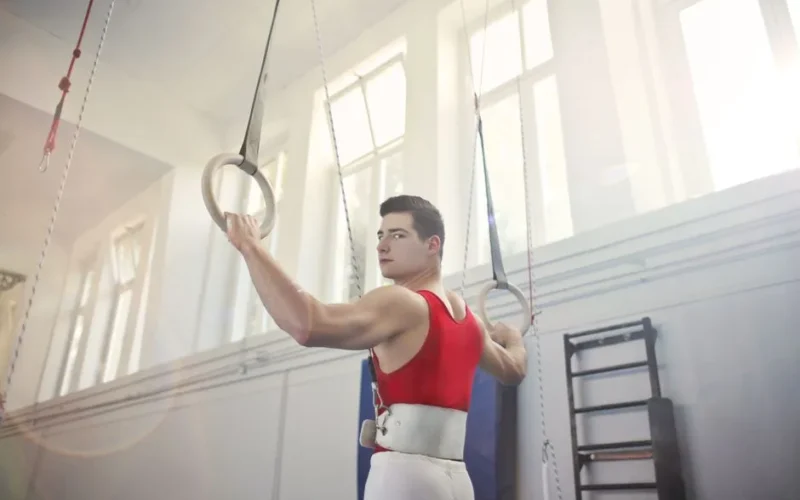 A male gymnast improves strength training on gymnastic rings indoors.