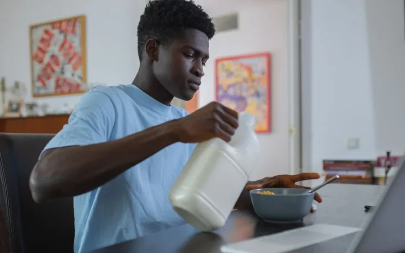 Teenager pouring milk into a bowl of cereal at home, enjoying breakfast.