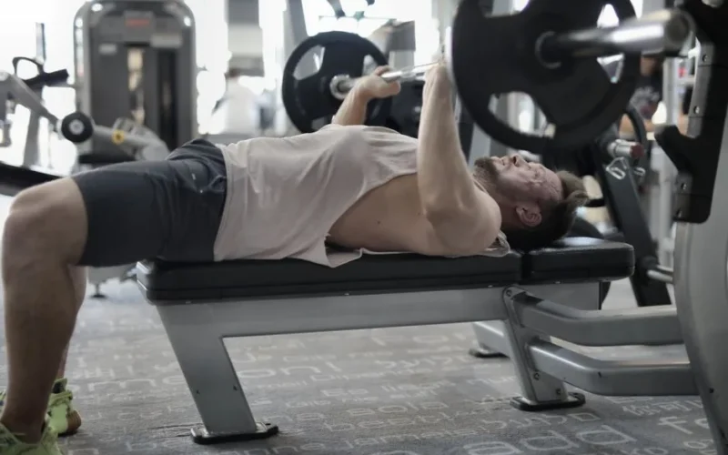Side view of strong muscular sportsman in sportswear performing weightlifting exercise with heavy barbell on bench during intense workout in gym
