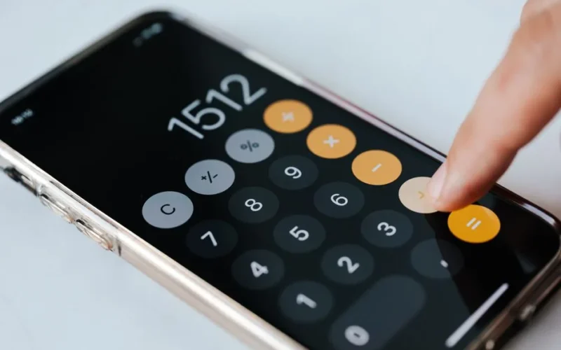 From above of crop faceless financier touching plus sign on screen of cellphone while using calculator application and calculating total amount