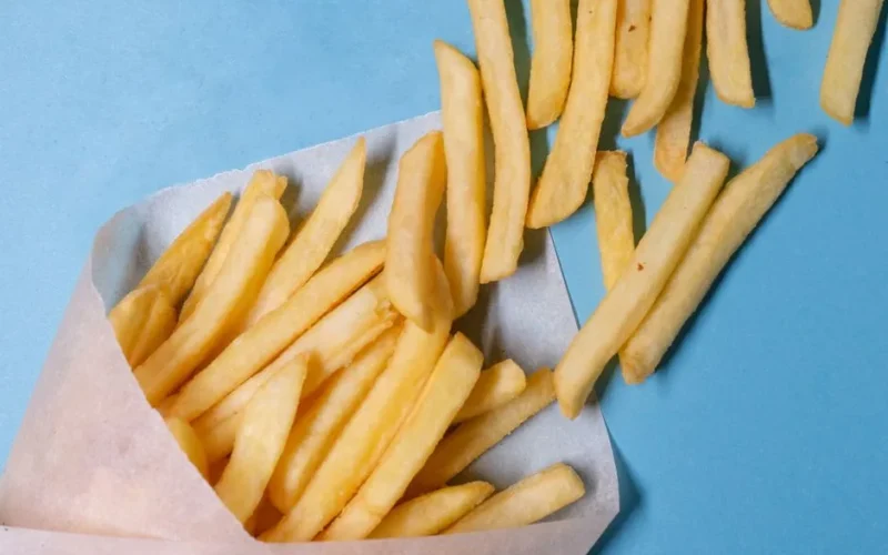 Top view of tasty french fries in paper placed on blue table in light studio