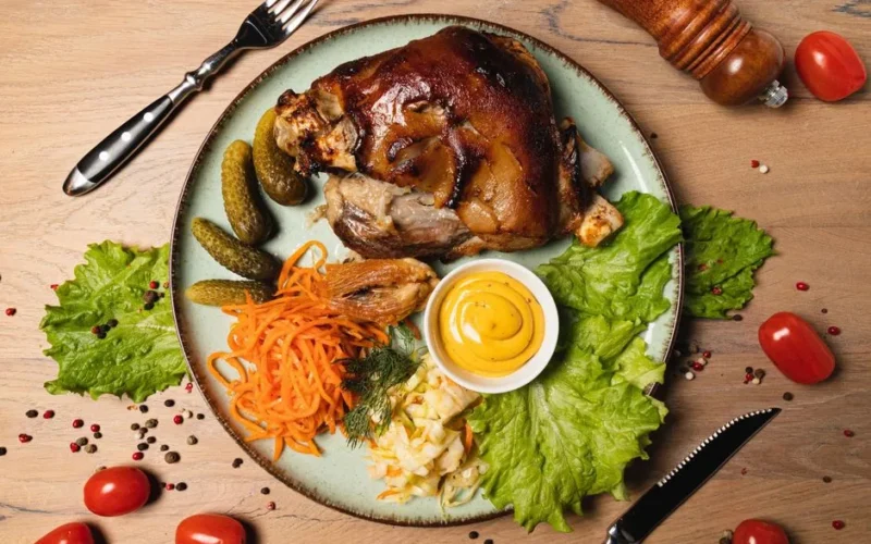 Top view of a delicious gourmet roast pork knuckle served with fresh vegetables and sauces on a rustic plate.