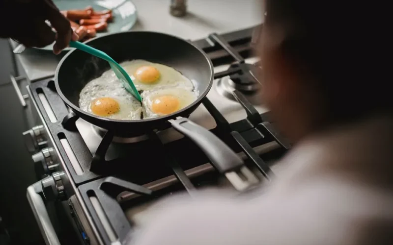 A person prepares fried eggs on a stove for breakfast, emphasizing home cooking and food preparation.